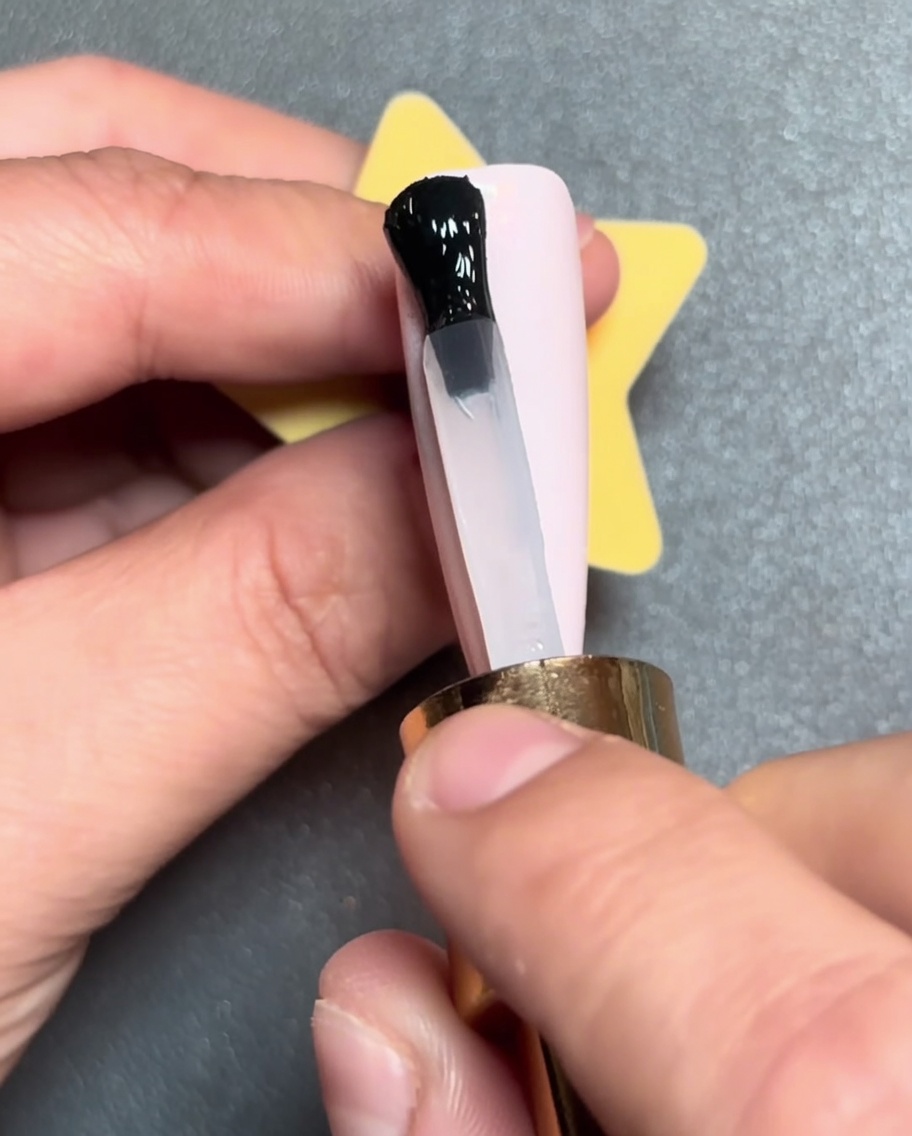 Un pincel aplicando una línea horizontal de esmalte en gel negro en la punta de una uña rosa.