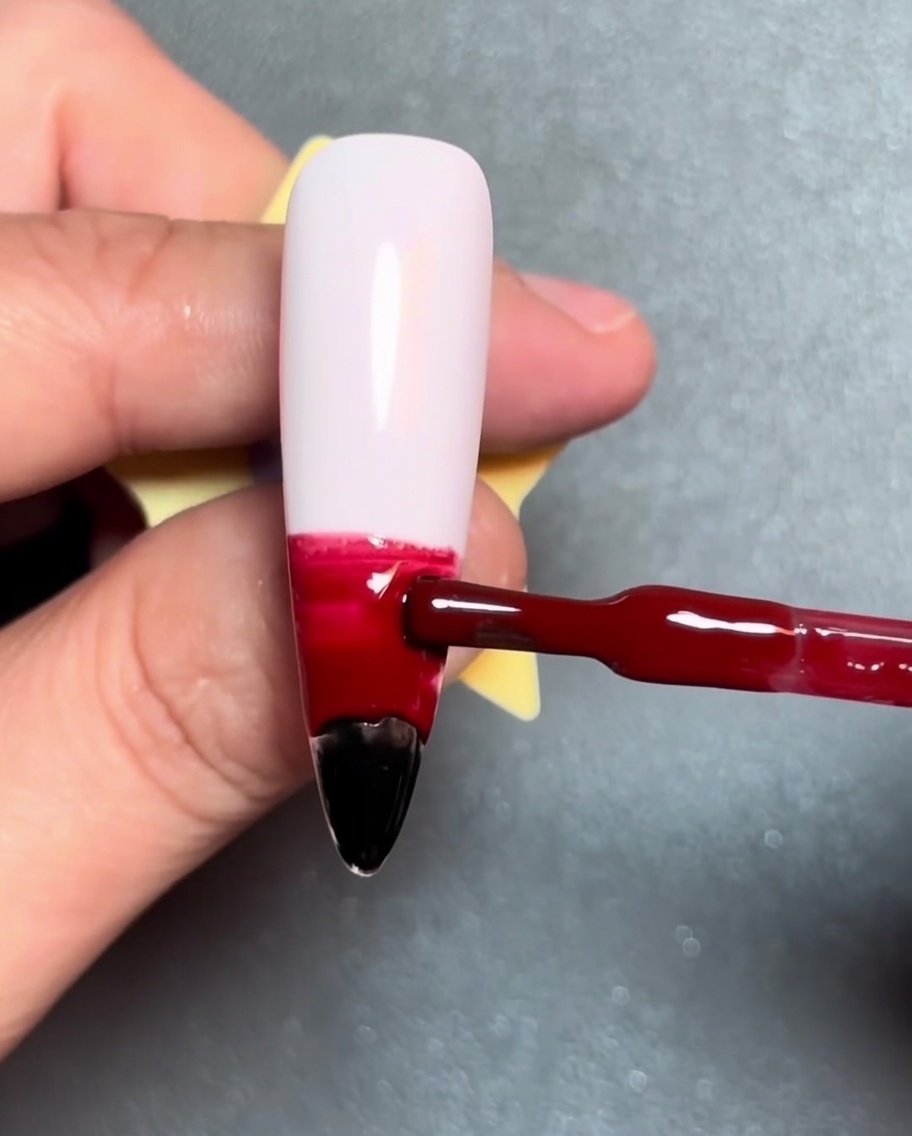 Un pincel aplicando una franja horizontal de gel naranja sobre el gel rojo.