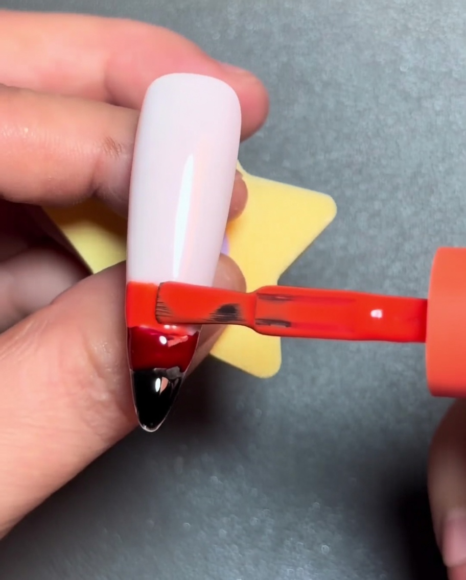 Un pincel trazando una línea de esmalte en gel amarillo sobre la franja de gel naranja.