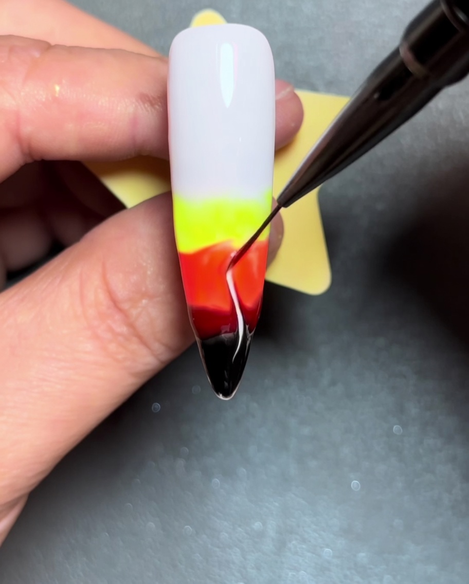 Primer plano que muestra un pincel liner arrastrando líneas de color hacia arriba a través del gel húmedo para crear formas de llama.
