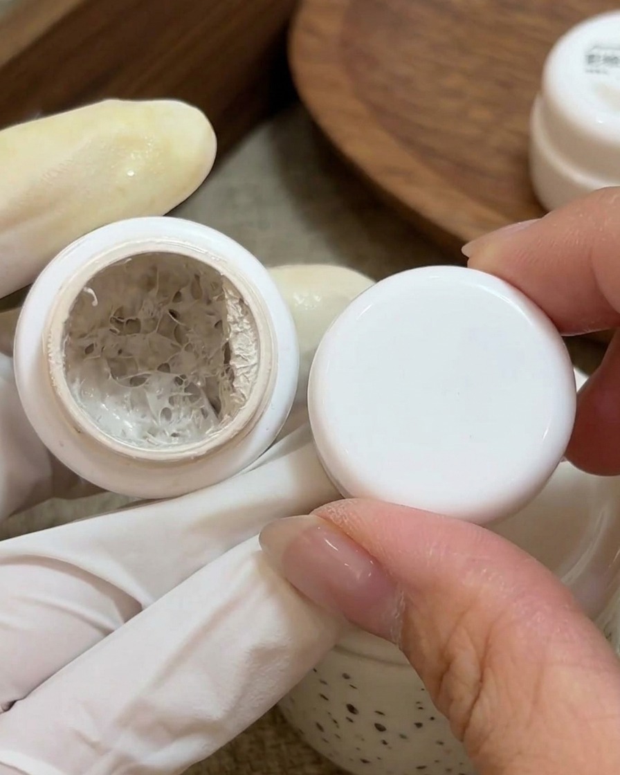 Un pincel pequeño aplicando gel de pintura blanco sobre la base de una uña natural preparada.