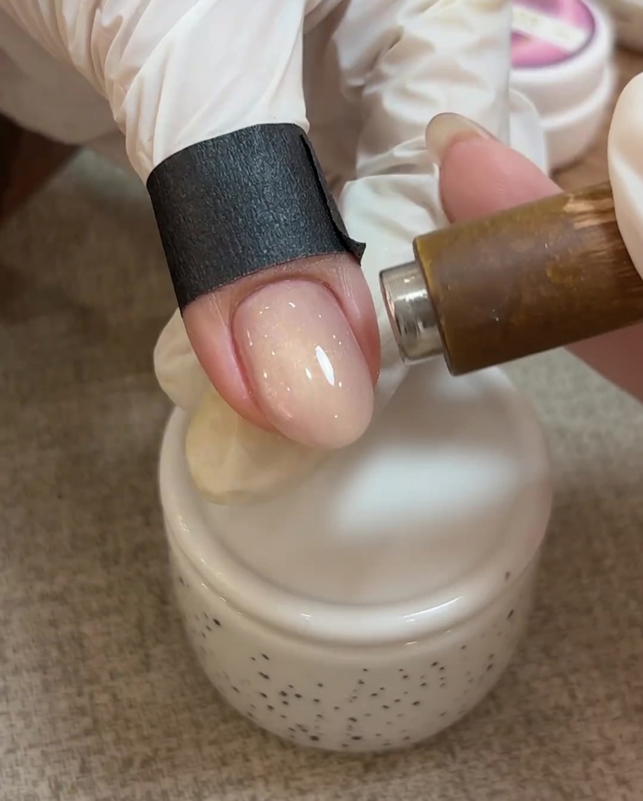 Vista de primer plano de un imán sobre una uña con gel cat eye sin curar, mostrando las partículas magnéticas creando una línea brillante.