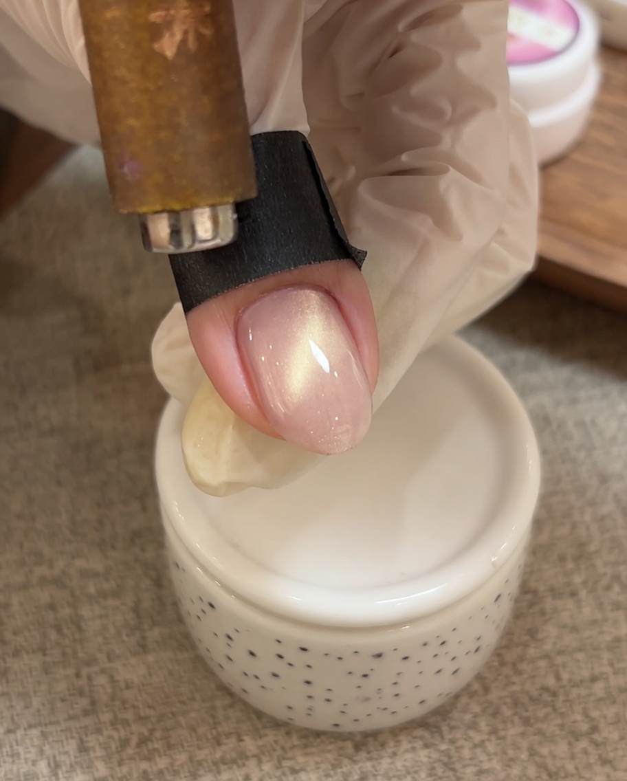 Una mano usando una herramienta magnética para empujar las partículas brillantes del gel cat eye hacia la punta de la uña.