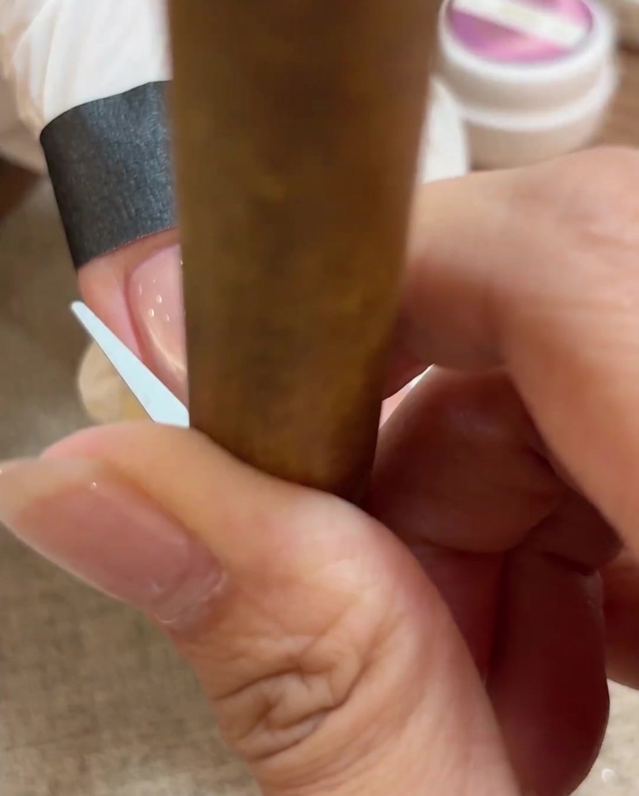 Primer plano de una herramienta pequeña usada para manipular el gel cat eye en un arco de punta francesa perfecto.
