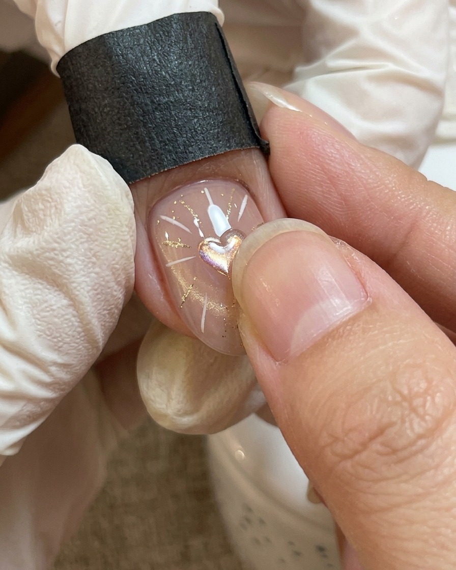 Vista de primer plano de un proceso de arte de uñas donde un gel transparente más espeso se coloca cuidadosamente sobre el motivo central del corazón.
