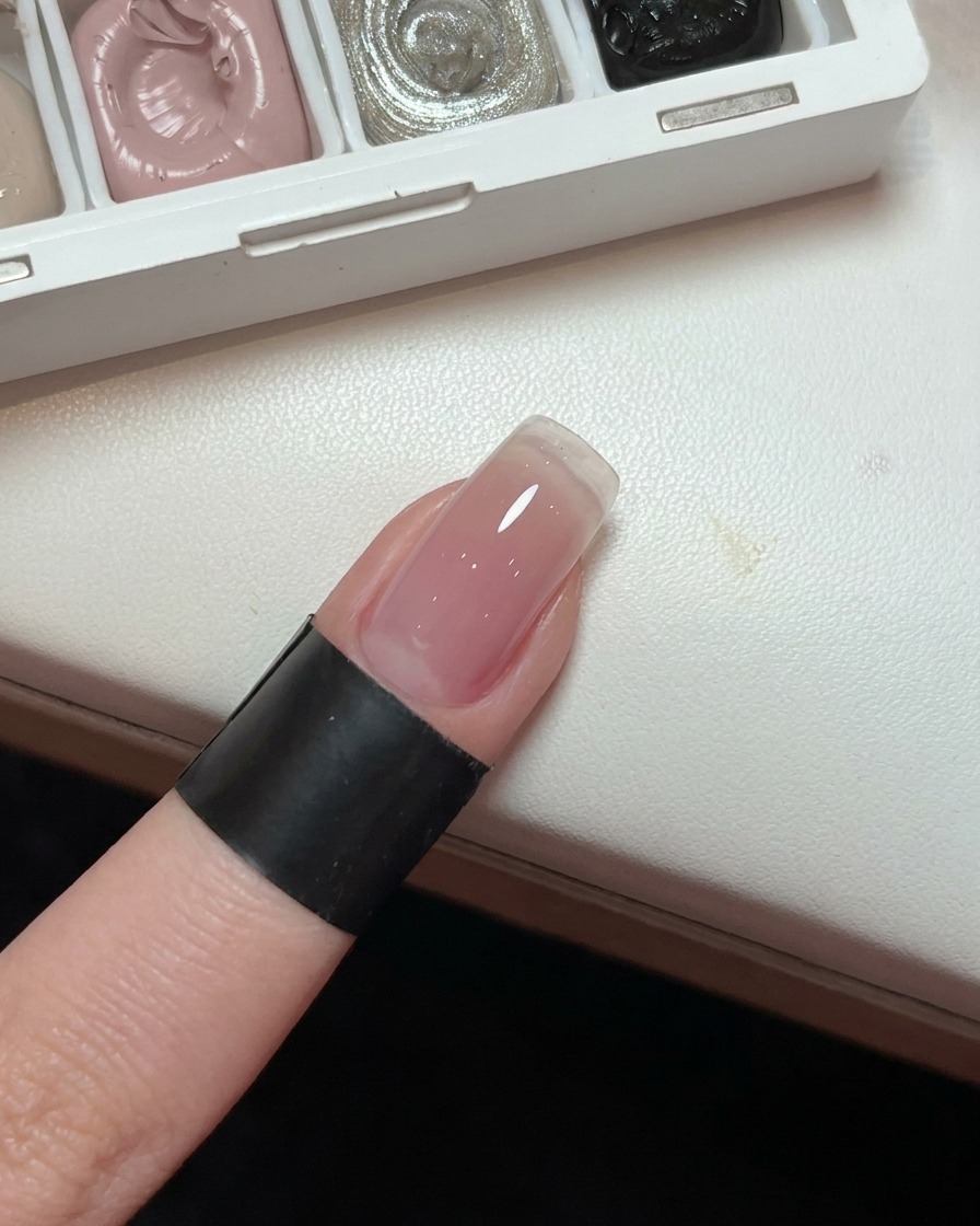Primer plano de una uña mostrando una base de gel degradada en rosa claro y suave.