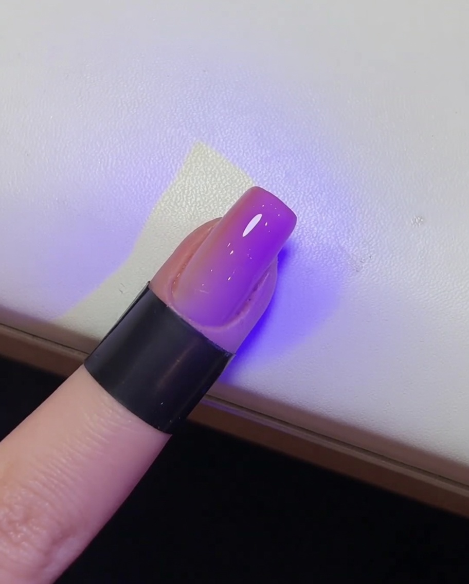 Primer plano de una uña brillante terminada siendo curada bajo una lámpara UV.