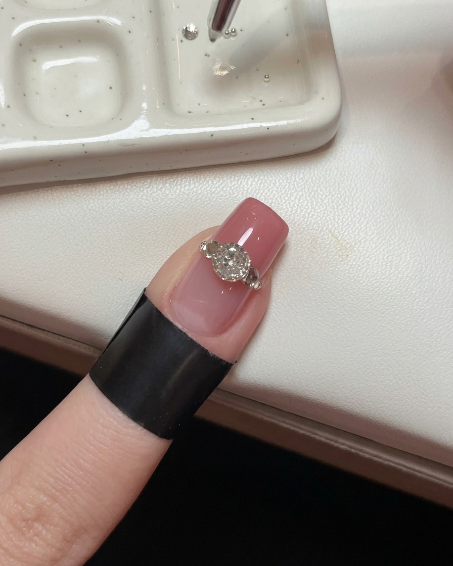 Primer plano de una uña con un cristal grande, mostrando una herramienta de precisión colocando pequeñas cuentas de acero alrededor de su base para crear un efecto de garra.