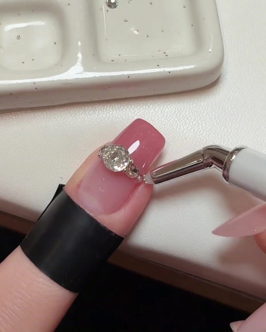 Una toma detallada del arte de uñas, mostrando una herramienta de precisión colocando cuentas de acero microscópicas en los pequeños espacios entre los cristales más grandes.