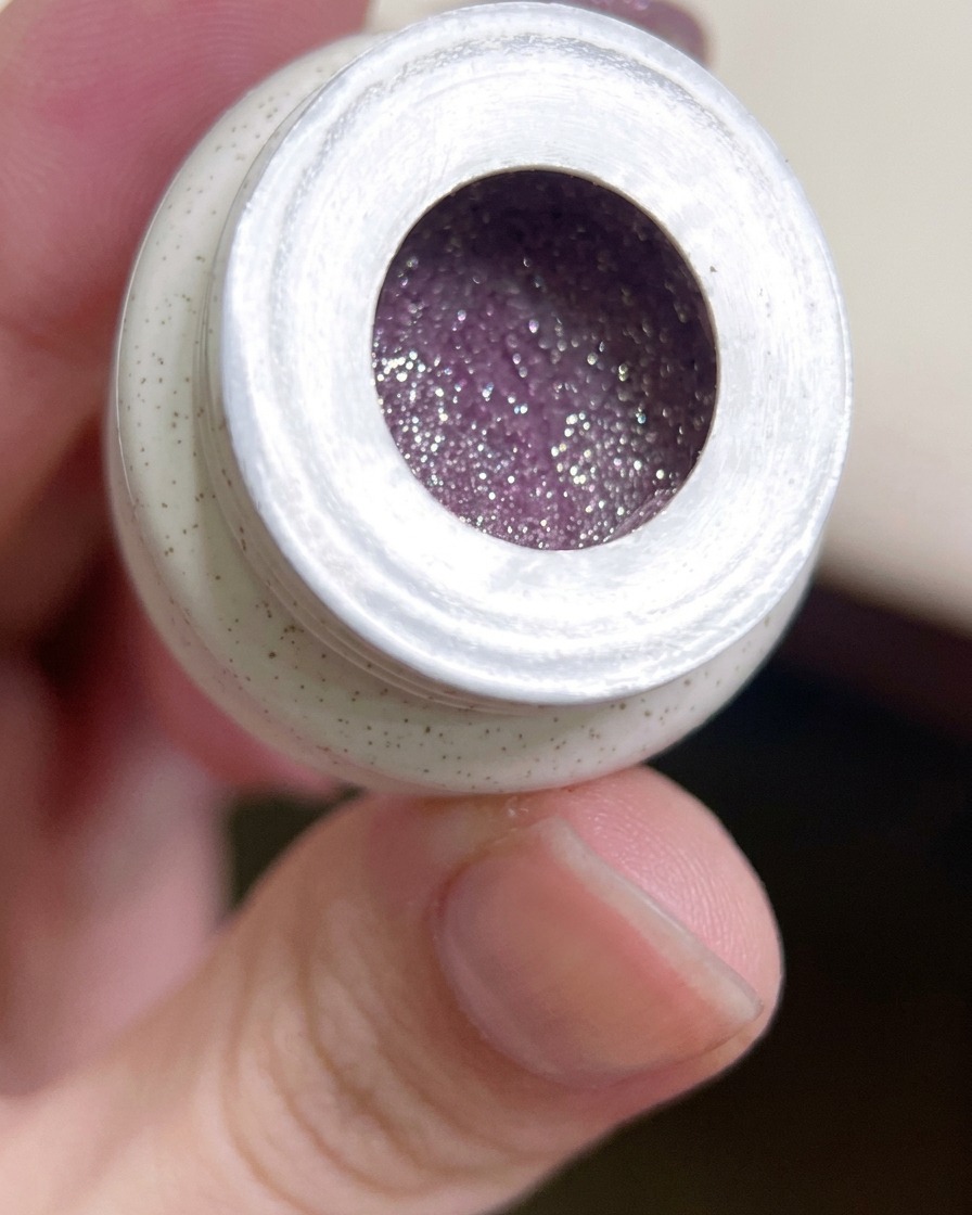 Un pincel plano de gel sumergiéndose en un frasco de gel de color morado con purpurina.