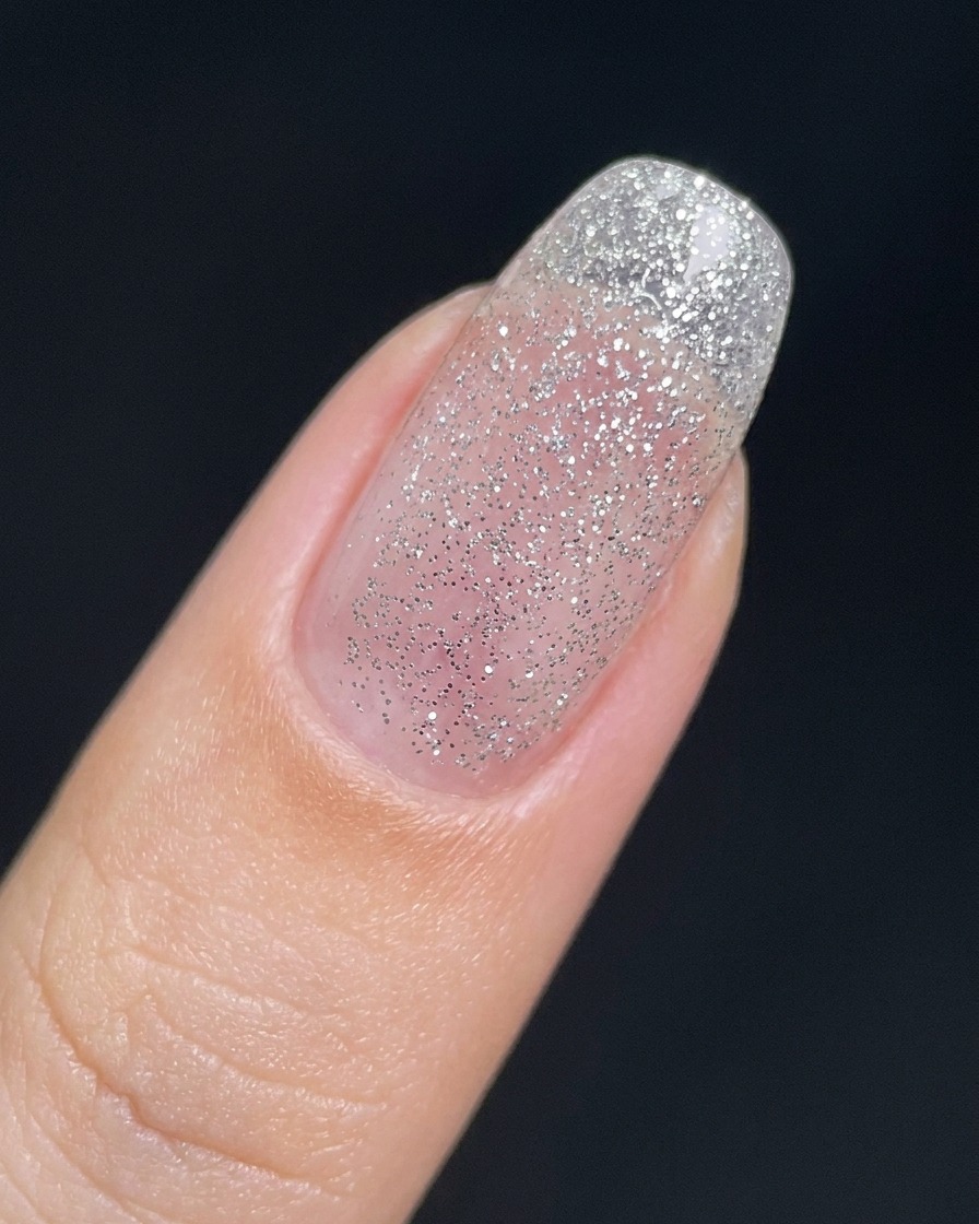 Una uña cubierta con una capa fina y transparente de gel con purpurina plateada.