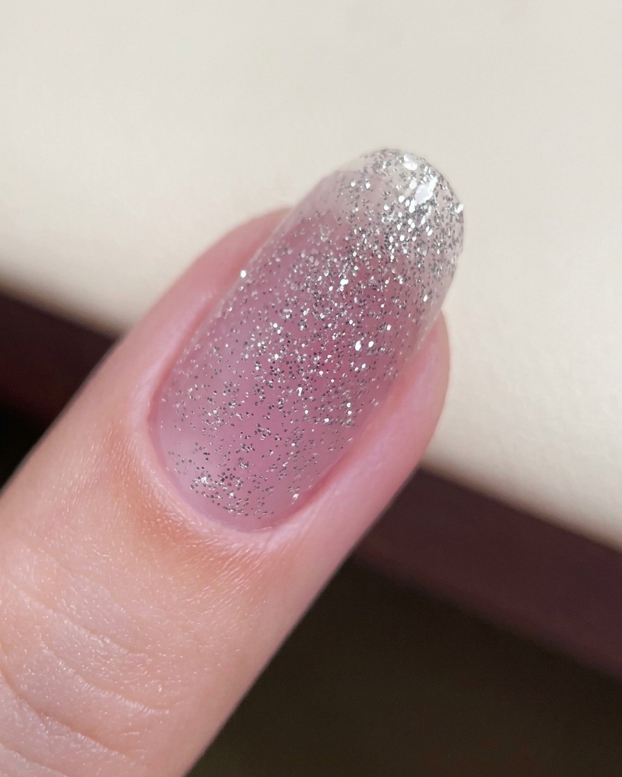 Primer plano de una uña con una capa base fina de gel con purpurina aplicada.