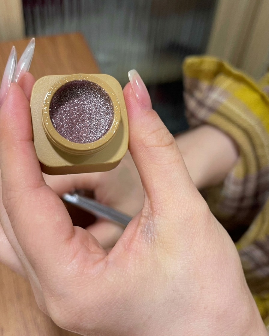 Vista en primer plano que muestra el gel con glitter rosa siendo aplicado en la base de la uña y difuminado hacia abajo.