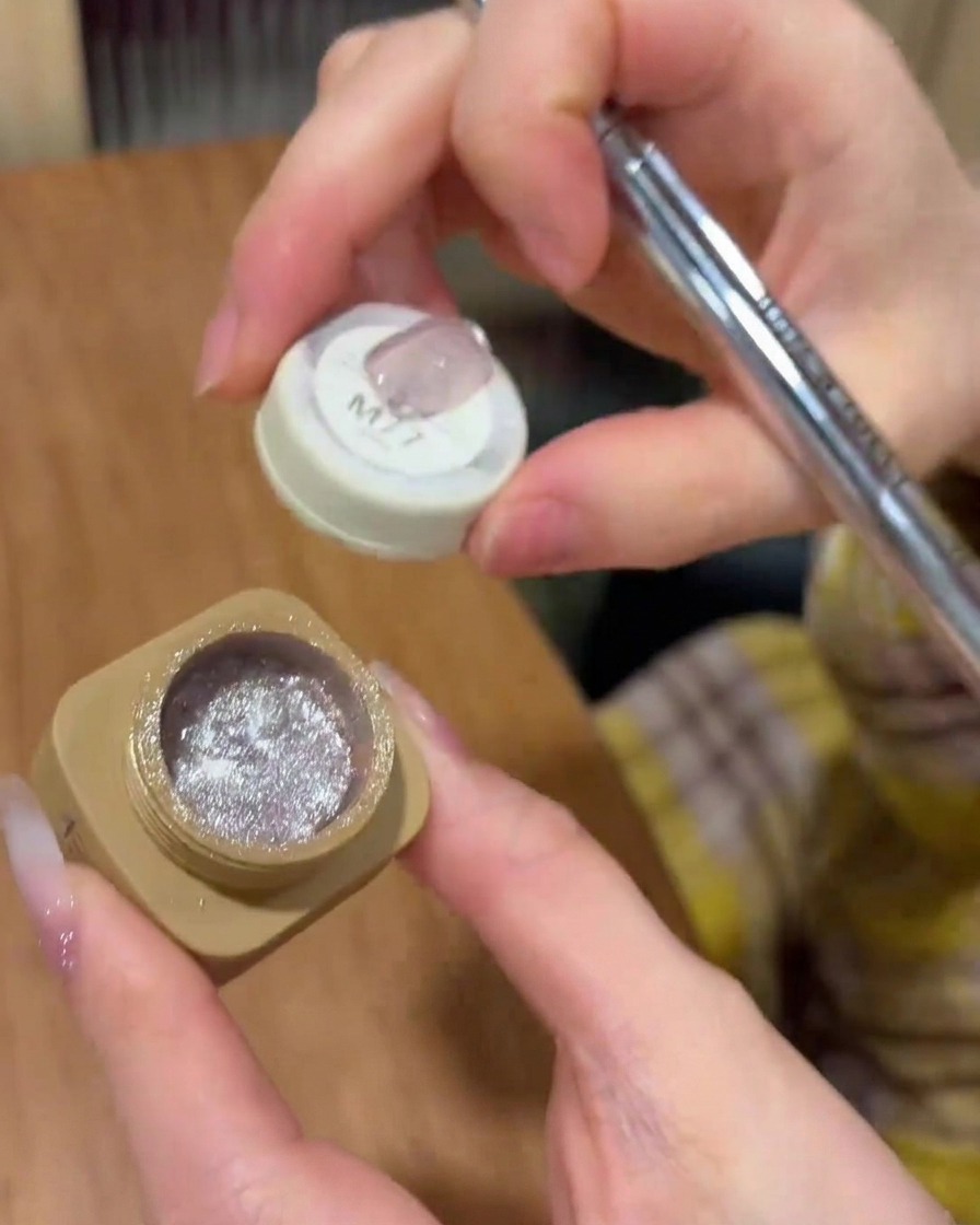 Un pincel aplicando esmalte de gel ojo de gato uniformemente sobre la superficie de la uña.