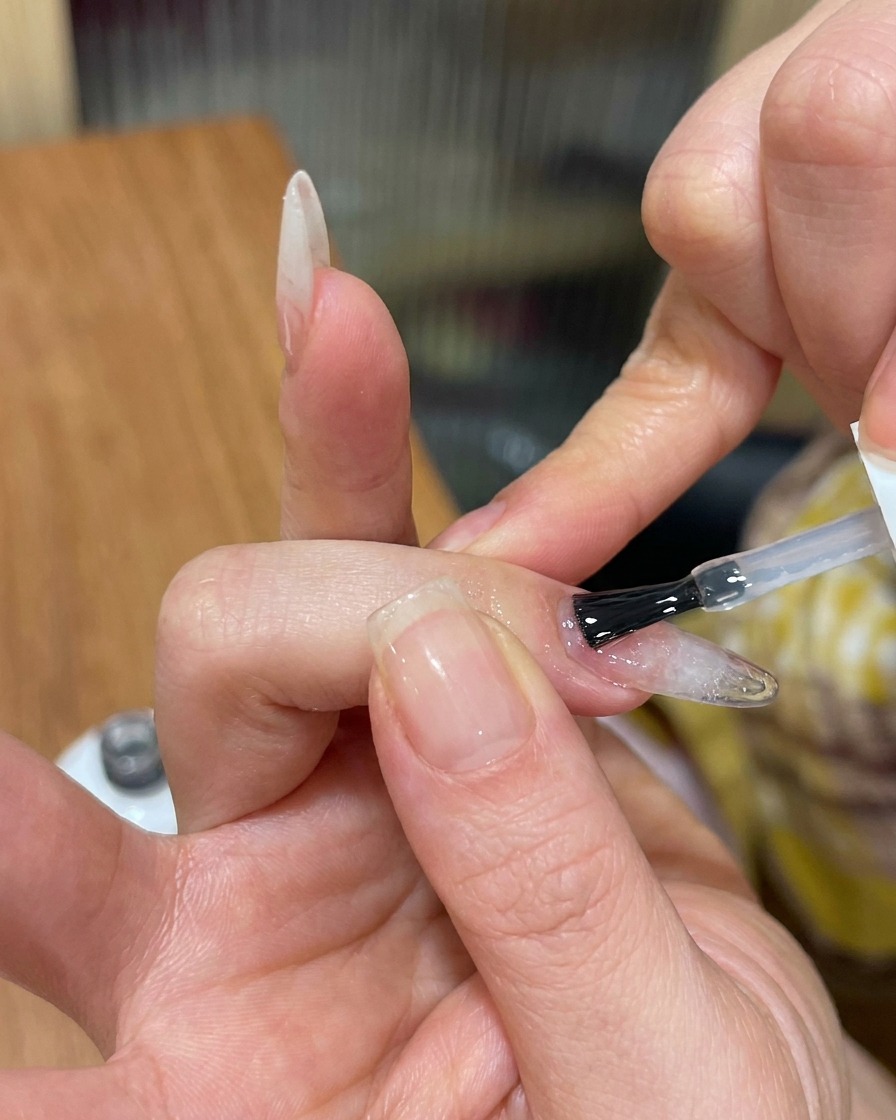 Un pincel aplicando un top coat transparente y brillante sobre una uña texturizada de gel ojo de gato.