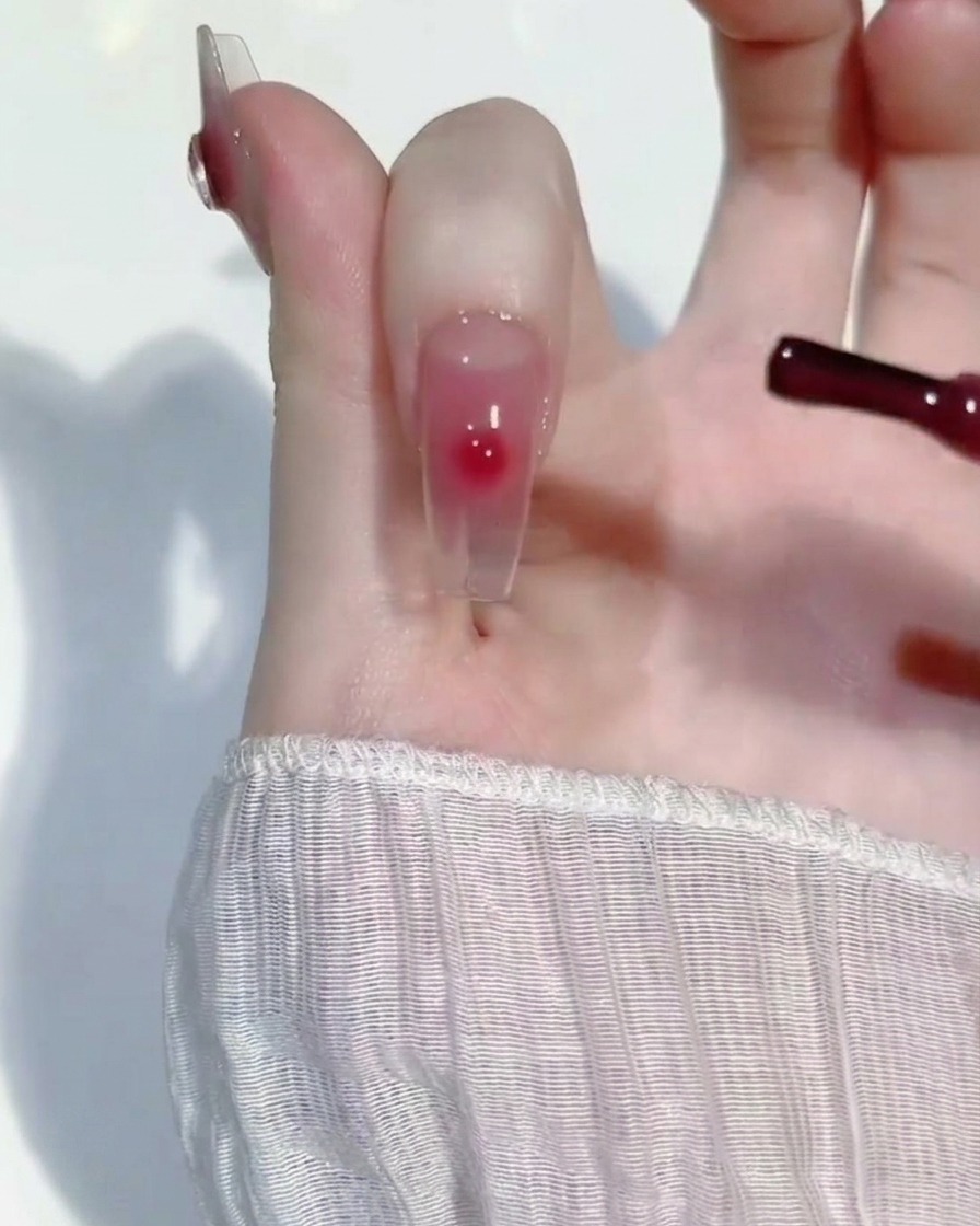 Una pequeña gota de gel rosa siendo difuminada en el centro de la uña con un pincel de detalle.