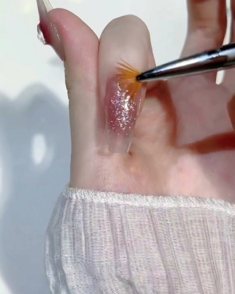 Un pequeño pincel de abanico pasando ligeramente sobre una capa húmeda de gel glitter en una uña para igualar la cobertura.