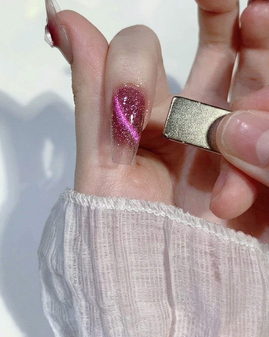 Un imán rectangular para uñas sosteniéndose al lado de una uña rosa con glitter, atrayendo las partículas magnéticas hacia una línea centrada.