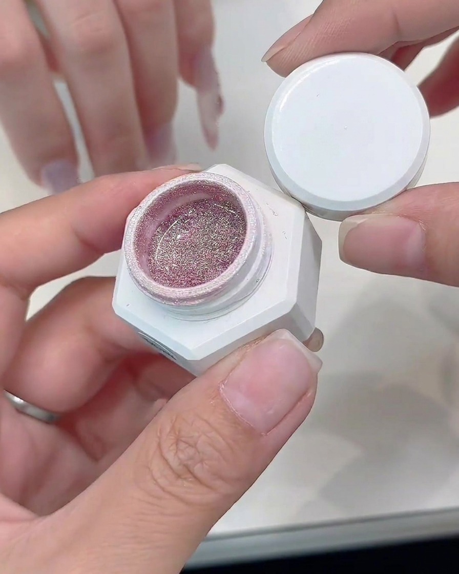 Un pincel de detalle aplicando gel de glitter plateado a lo largo del borde de una punta francesa cat-eye.