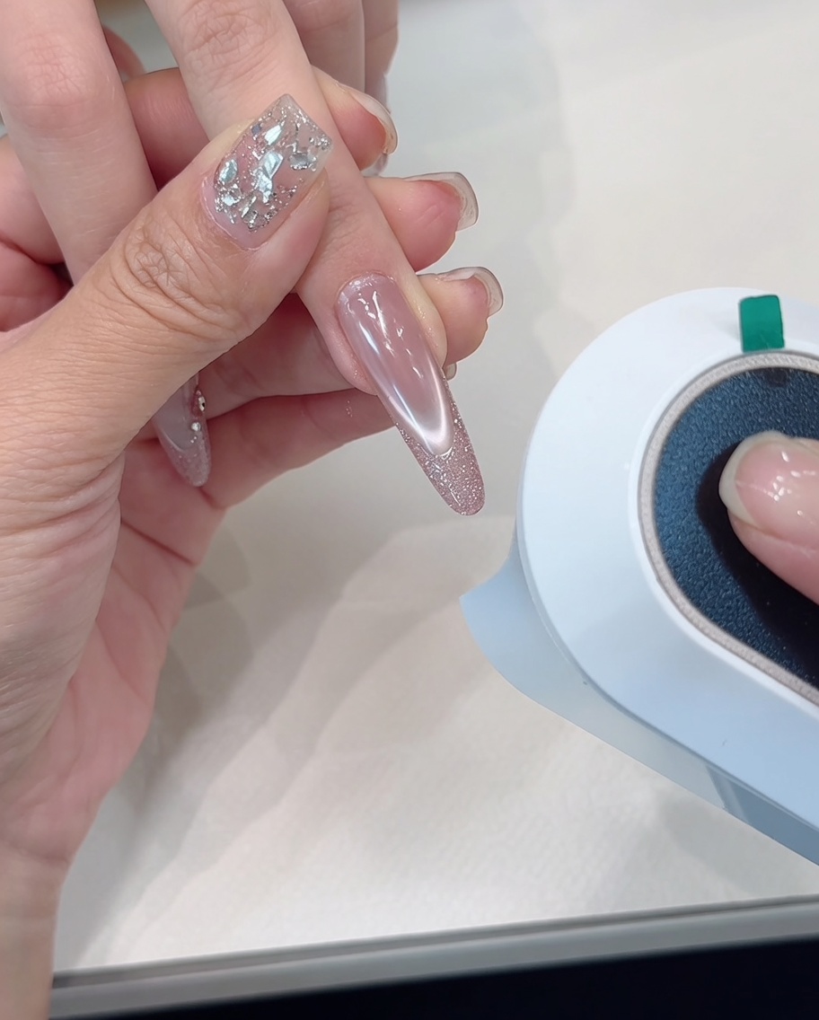 Una mano posicionada bajo una lámpara de curado, enfocada en las uñas con punta de glitter.