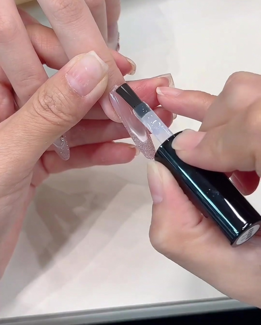 Un top coat transparente siendo aplicado sobre el diseño francés de glitter terminado.