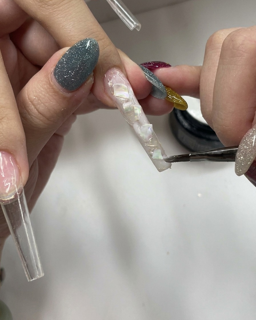 Un pincel aplicando una capa de gel blanco lechoso traslúcido sobre una superficie texturizada con conchas.