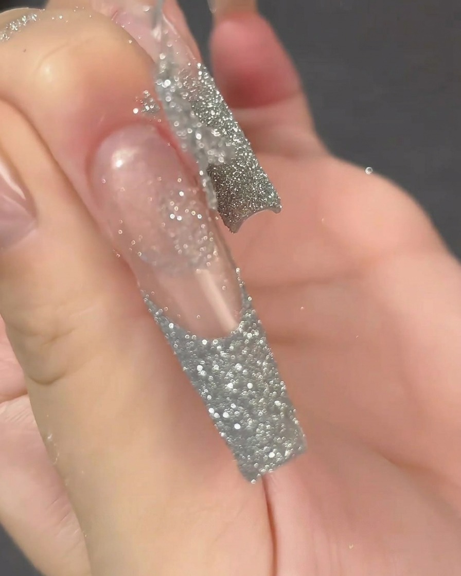 Primer plano de una toallita sin pelusa limpiando la superficie de una extensión de uña larga, transparente y preparada.