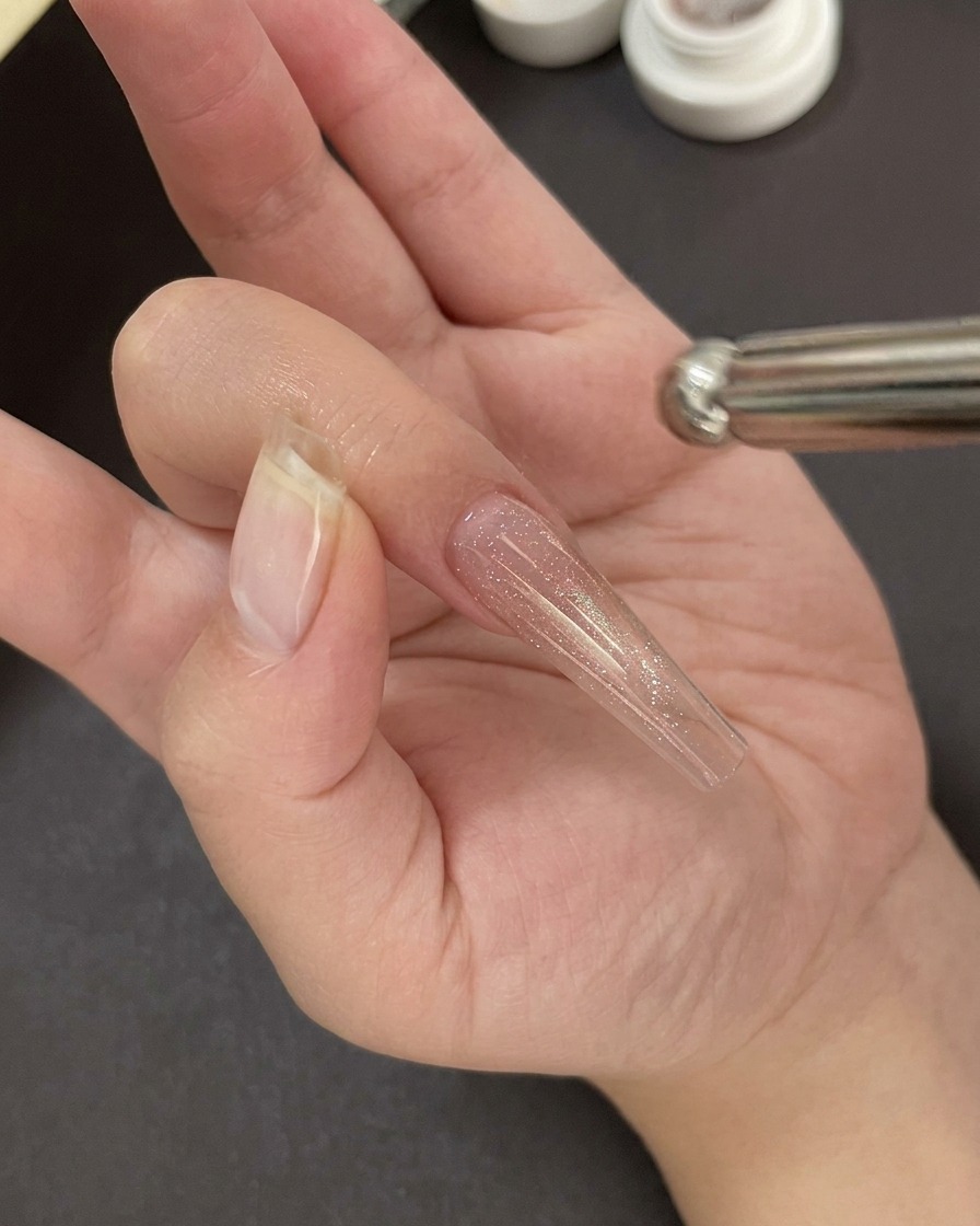 Una mano posicionada bajo una lámpara profesional de uñas UV/LED curando la base de gel.