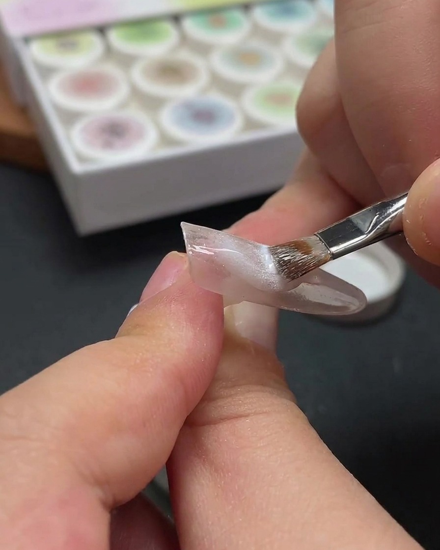 Primer plano mostrando una varita magnética flotando sobre una uña para desplazar las partículas metálicas en el gel húmedo.