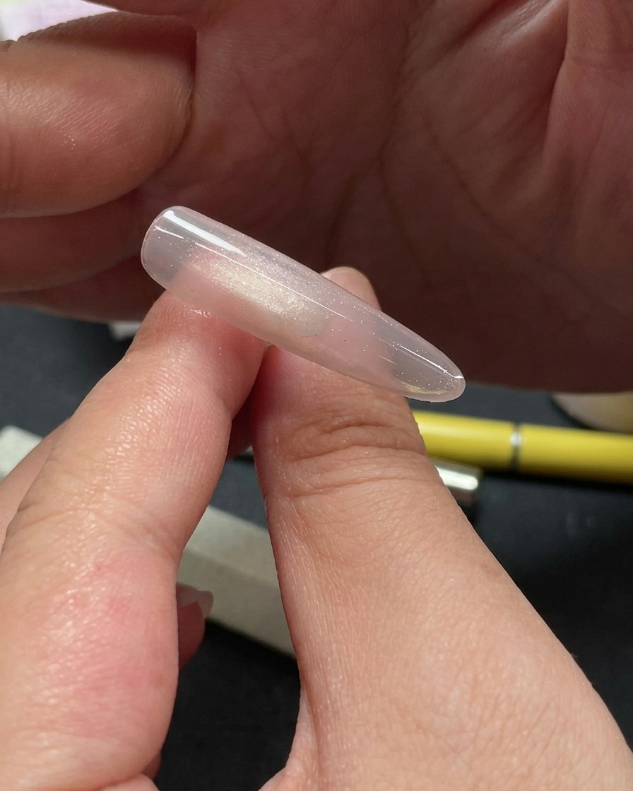 Primer plano de una mano usando una herramienta para colocar pequeñas piezas de purpurina brillante en la parte superior de una uña con gel ojo de gato.