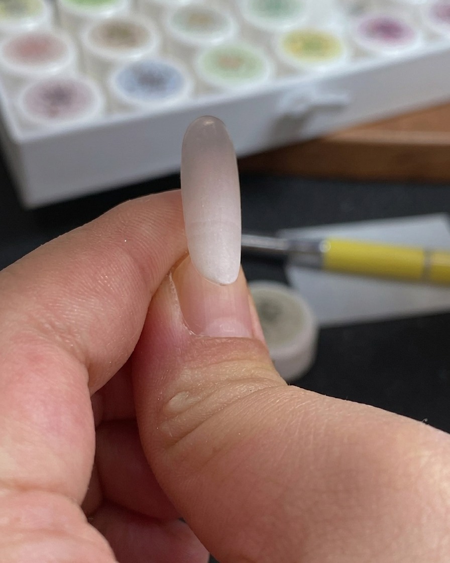 Primer plano de una esponja siendo presionada sobre la punta de una uña para crear un degradado suave de rojo rosado y blanco.