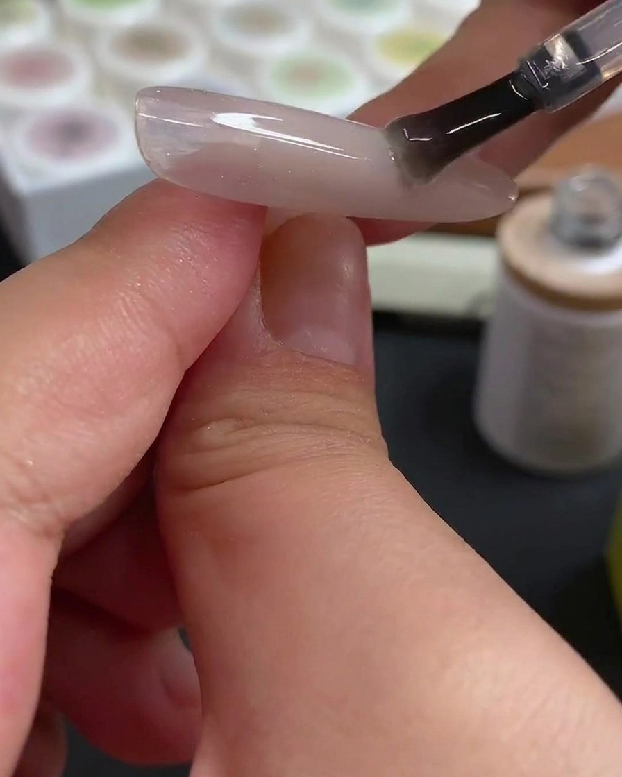 Una herramienta de punzón aplicando puntos precisos de gel rojo rosado sobre una superficie de uña preparada.