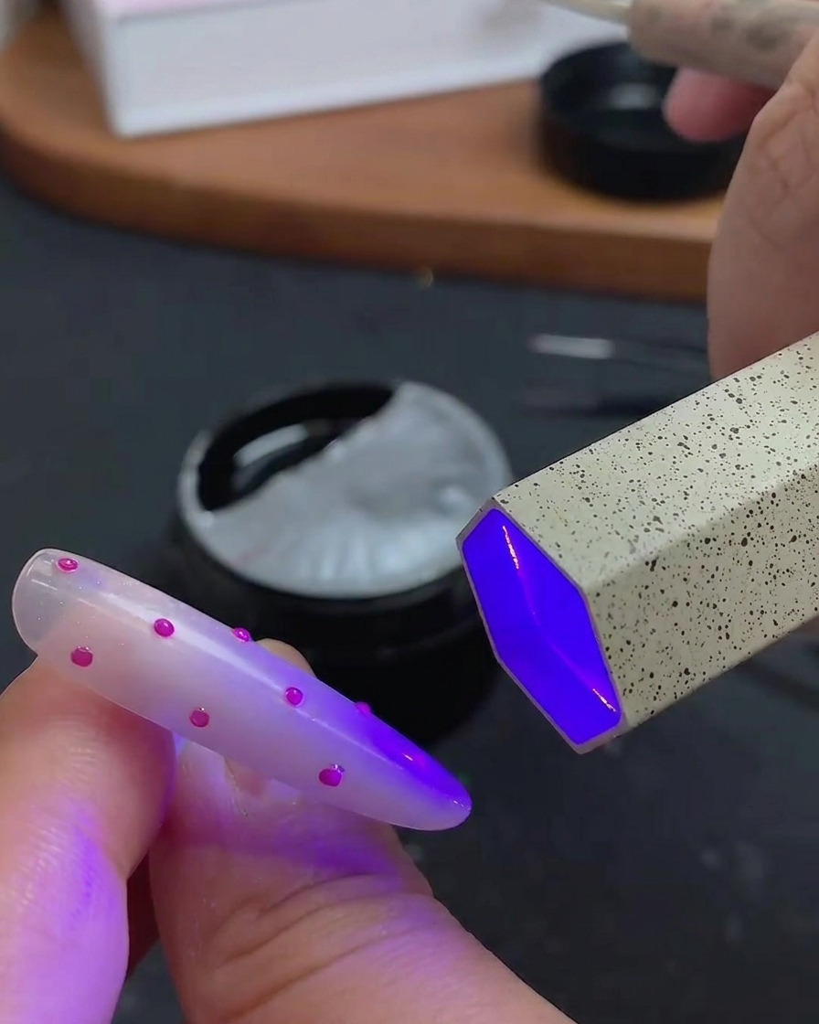 Un pincel aplicando una capa superior transparente y brillante sobre el arte de uñas de lunares en 3D.