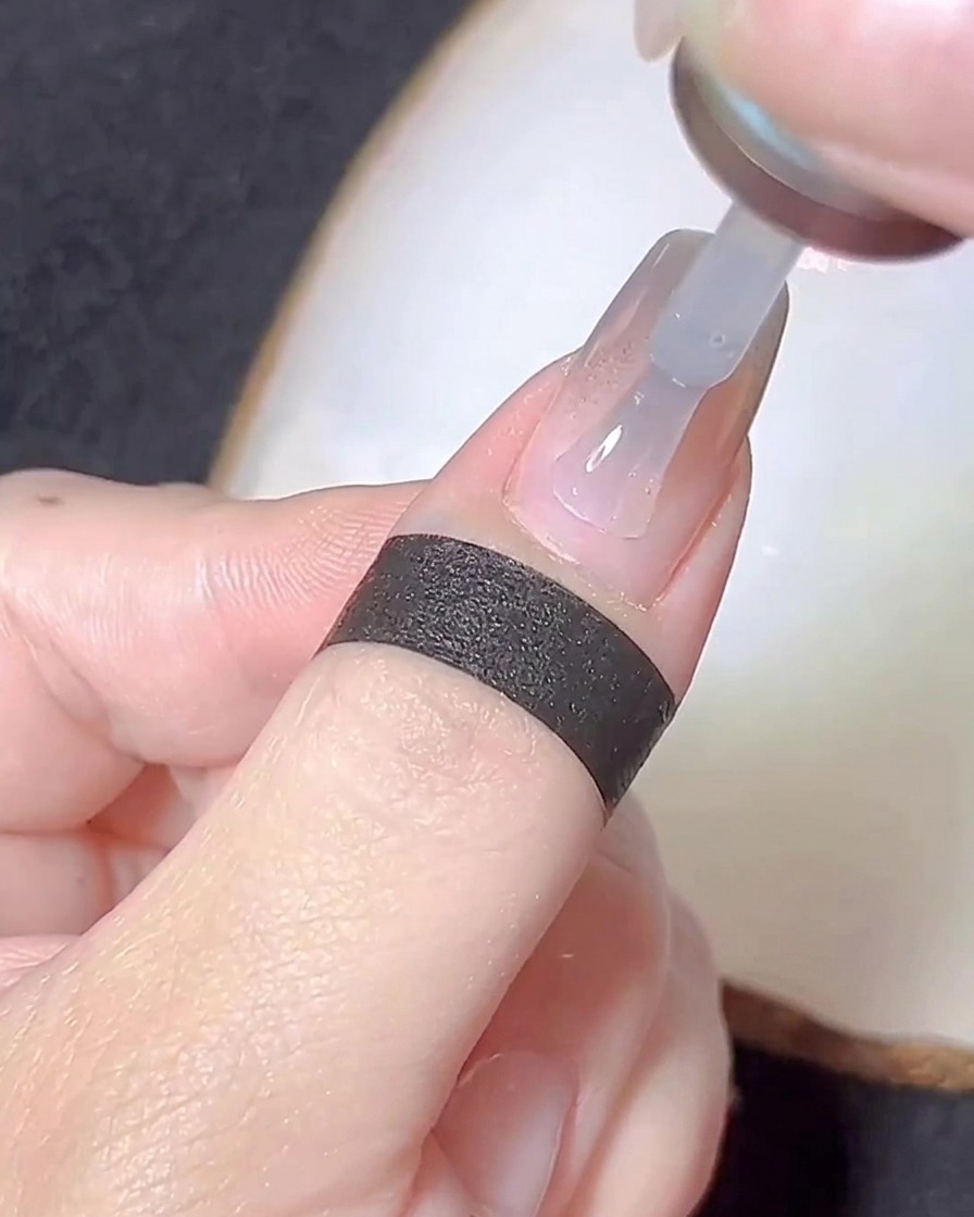 Un pincel aplicando una capa fina de gel base transparente sobre una uña con polvo cromo.