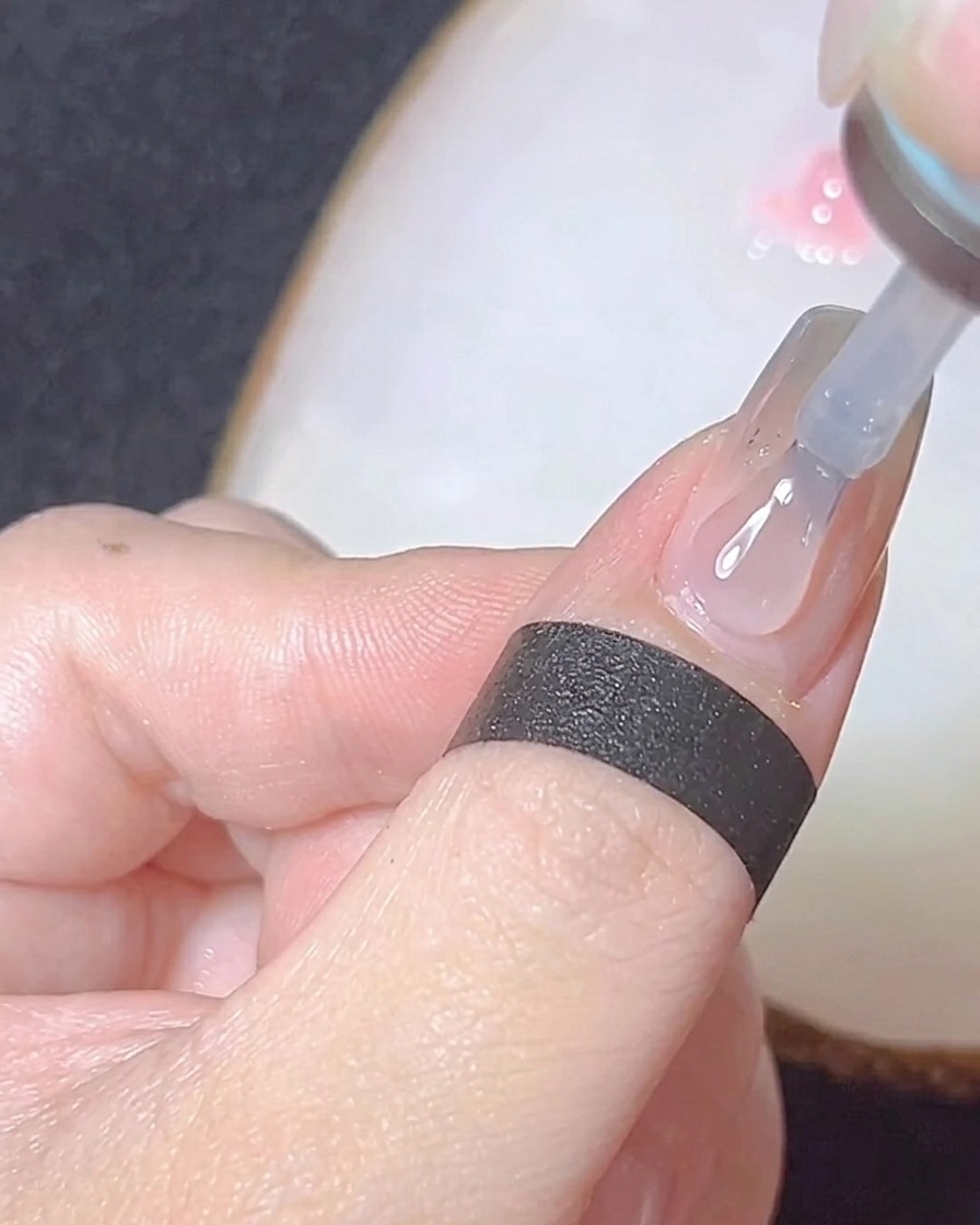 Primer plano de un pincel aplicando un top coat brillante sobre una uña con acabado cromo.