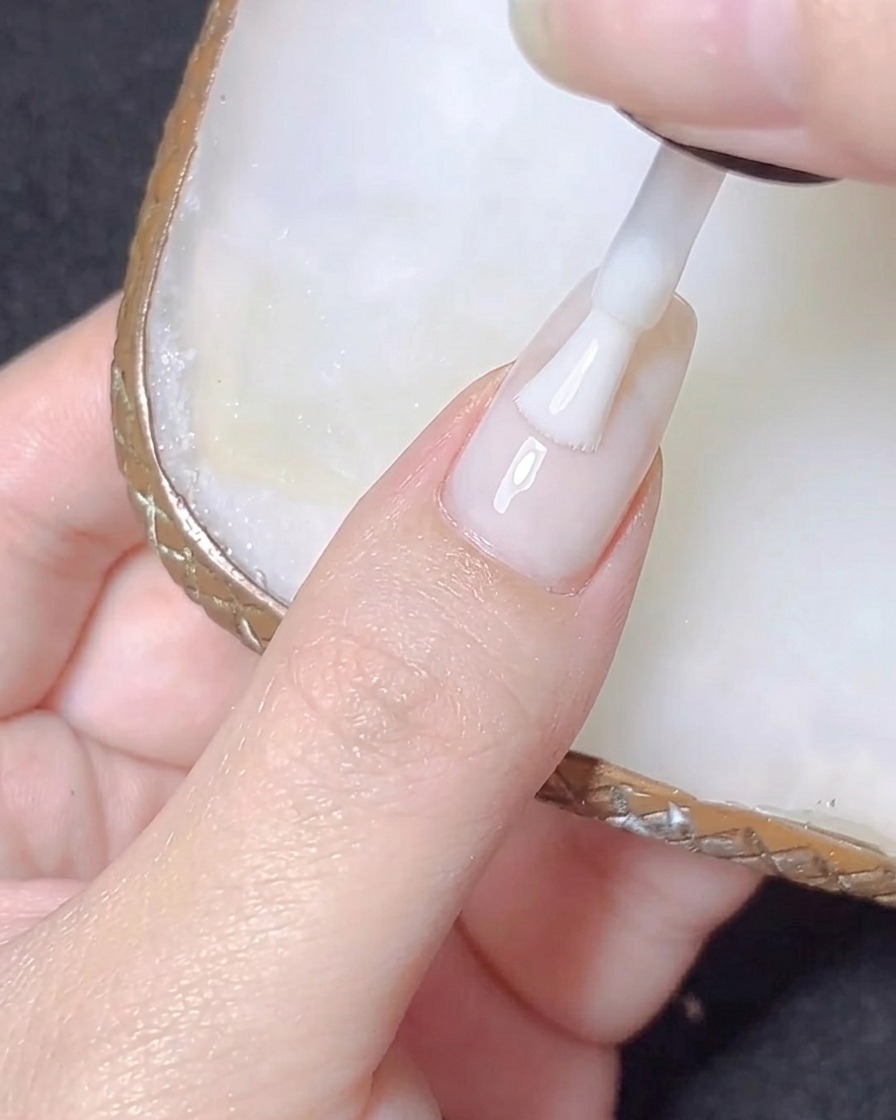 Un tip de extensión de uña transparente en forma almendrada siendo presionado sobre una uña natural.