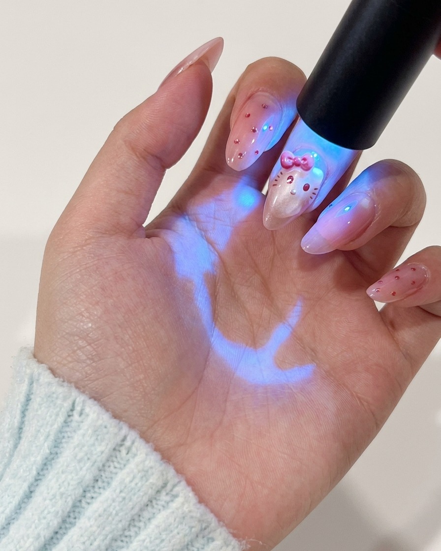 Una mano sosteniendo una lámpara UV sobre la uña para curar el diseño de personaje pintado en rojo.