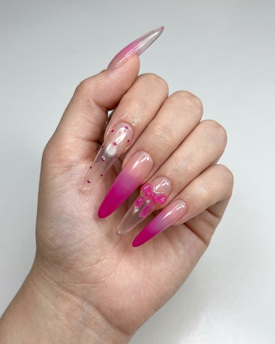 Un par de pinzas colocando un pequeño dije de lazo rosa 3D sobre la superficie de una uña manicurada.