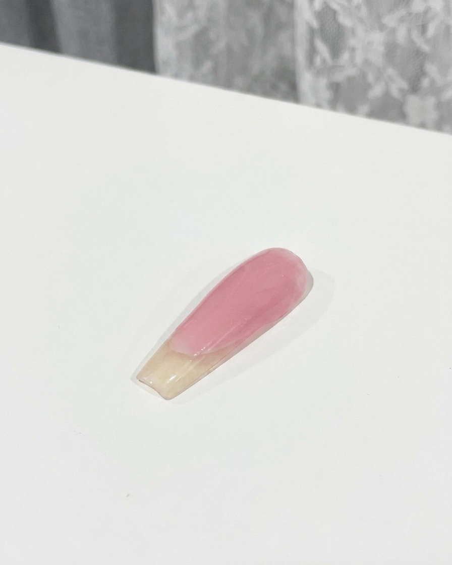 Un pincel aplicando una capa de top coat sobre un dije de lazo rosa 3D fijado en una uña.