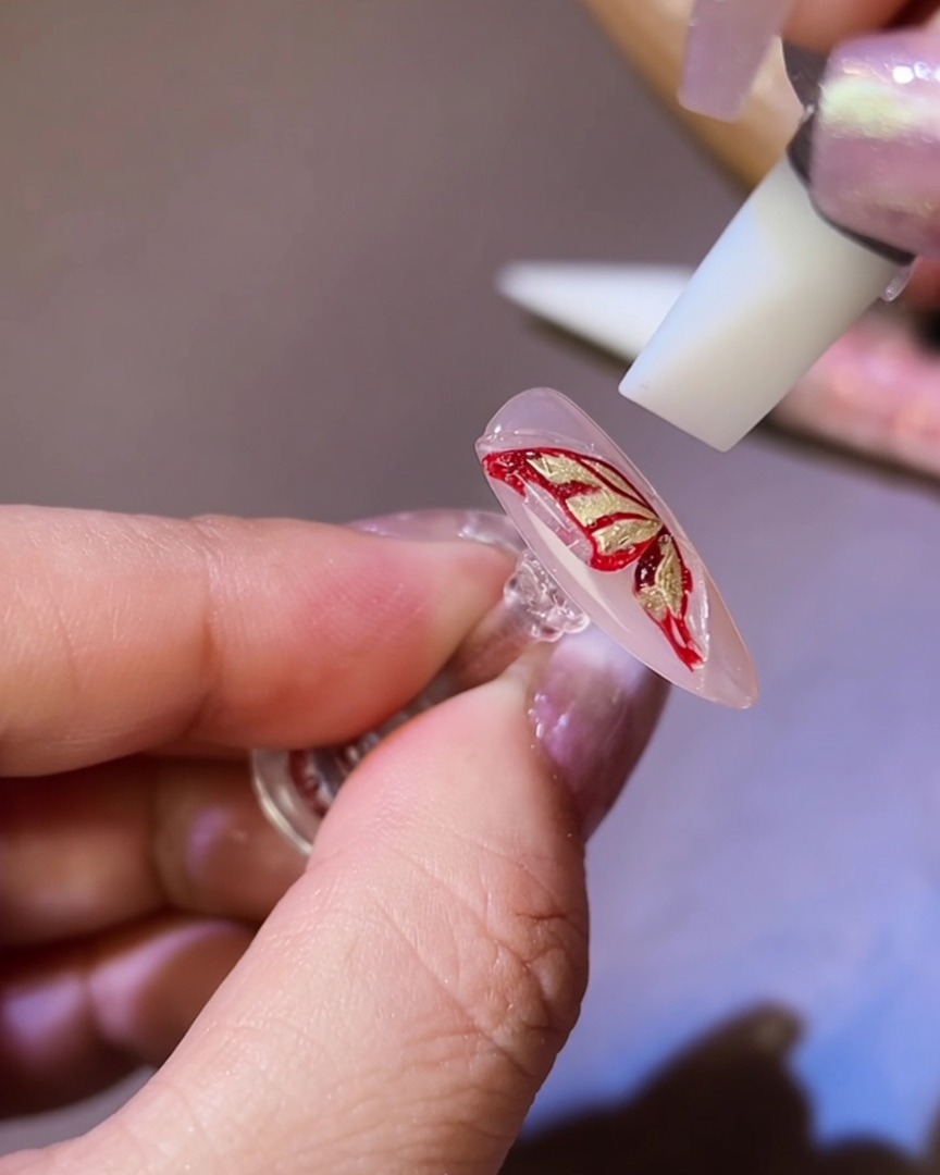 Una herramienta de silicona dando forma al gel 3D en una silueta de ala de mariposa sobre la uña.