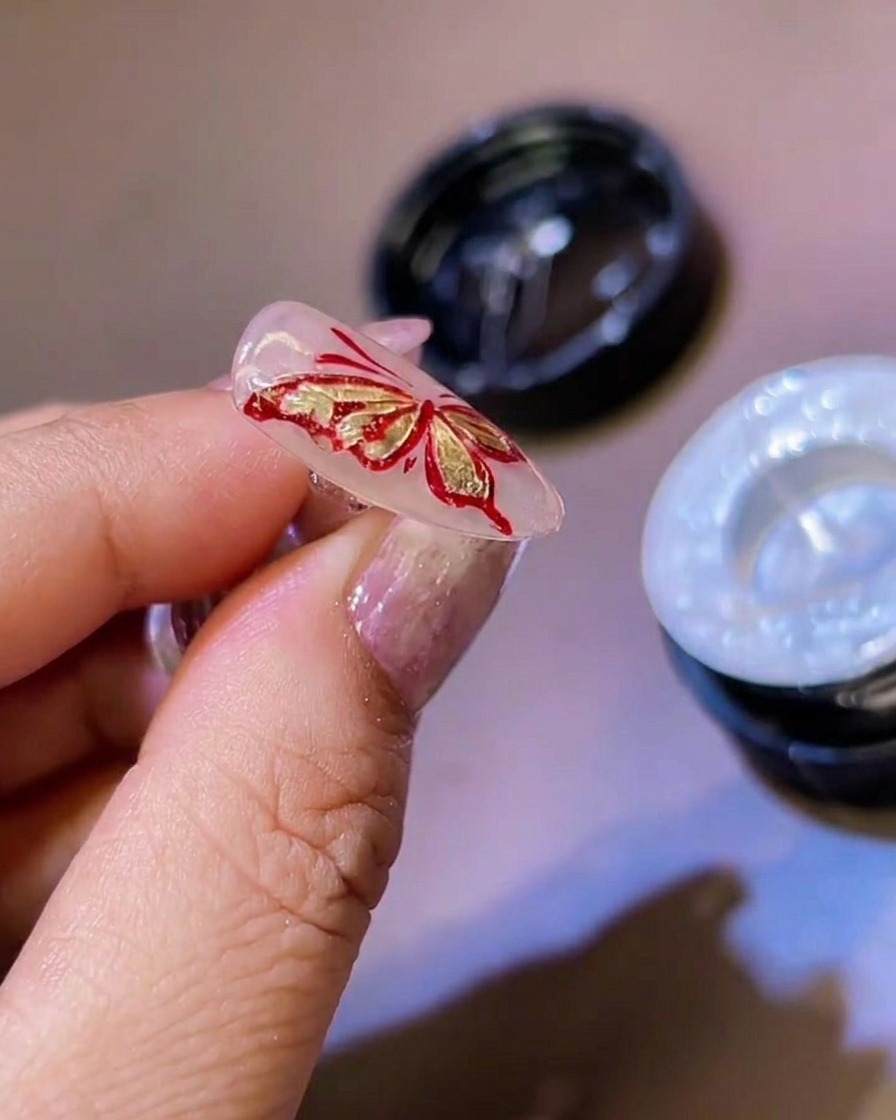 Un pincel fino delineador añadiendo detalles finos de gel blanco a los bordes de las alas de mariposa 3D.
