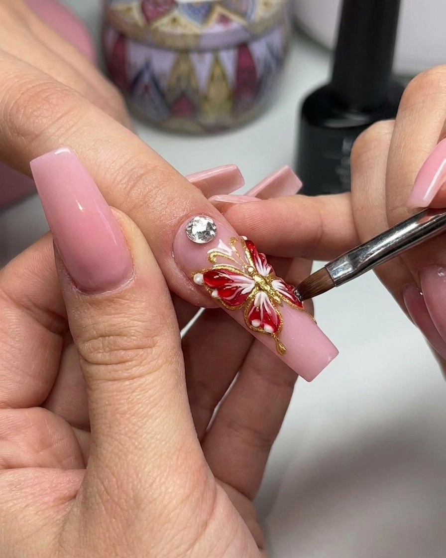 Pinzas colocando un adorno de cristal brillante en el centro de un diseño de uña de mariposa 3D.