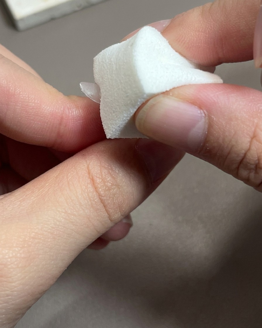 Un primer plano de un pincel aplicando un esmalte de gel rosa traslúcido sobre una uña.