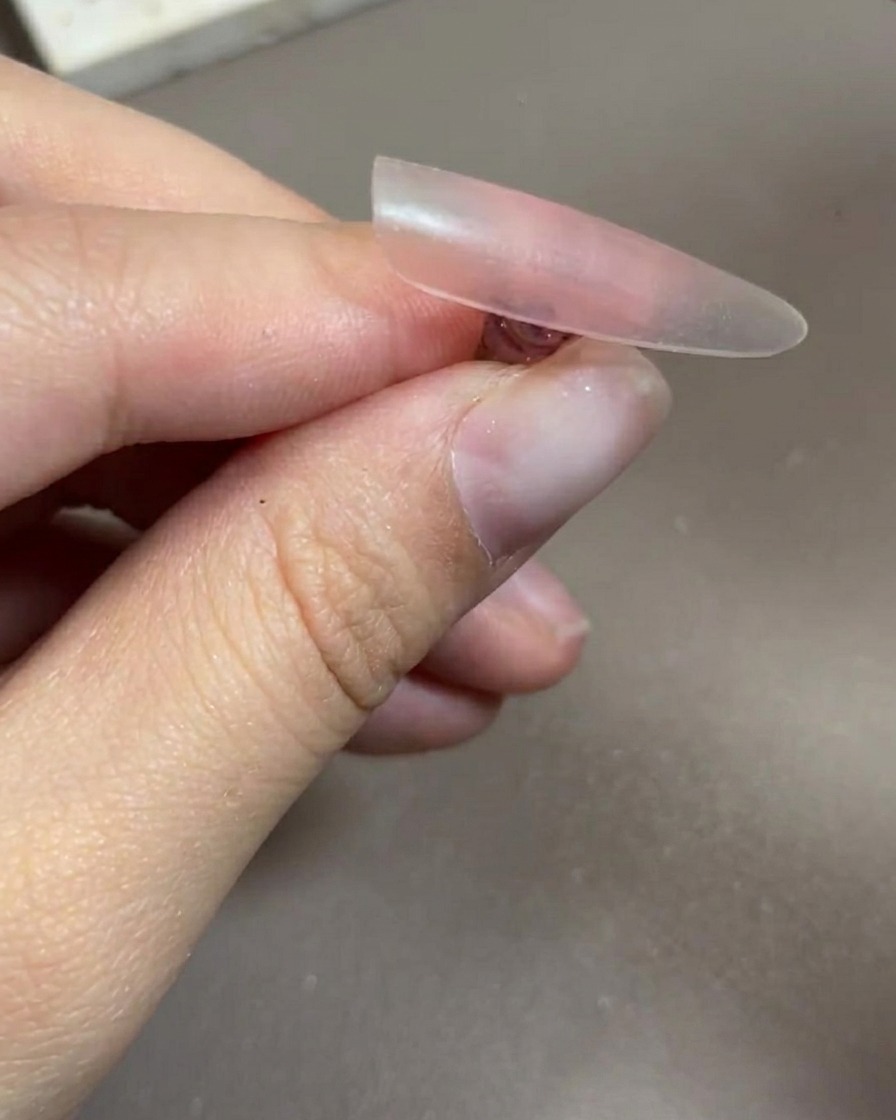 Una mano colocada dentro de una lámpara profesional de uñas UV/LED, con las uñas claramente visibles bajo la luz.