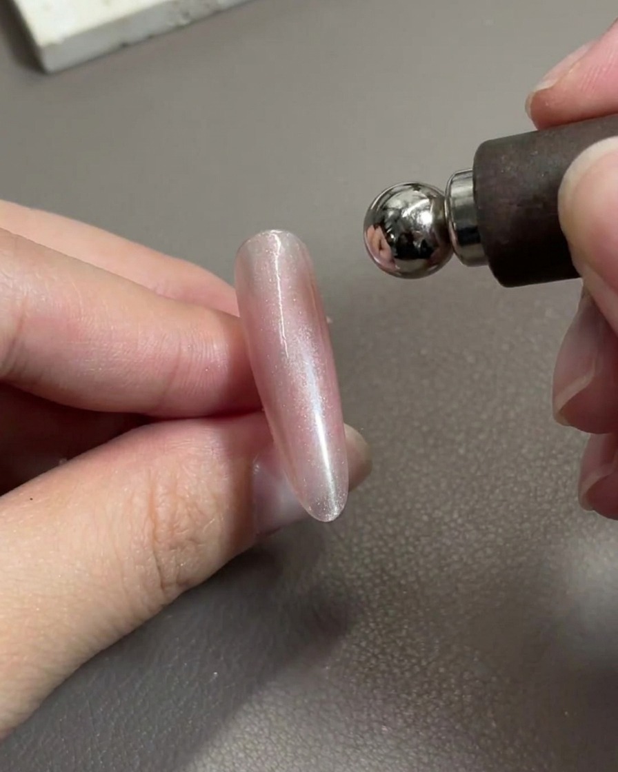 Una herramienta magnética de uñas posicionada sobre una uña de gel rosa brillante, desplazando activamente las partículas metálicas.