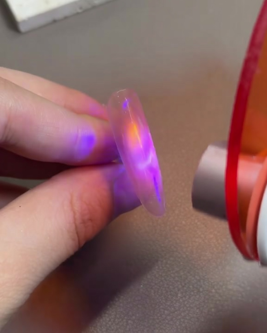 Un dedo con gel cat eye rosa siendo sostenido bajo una pequeña lámpara LED de mano para fijar el diseño magnético.