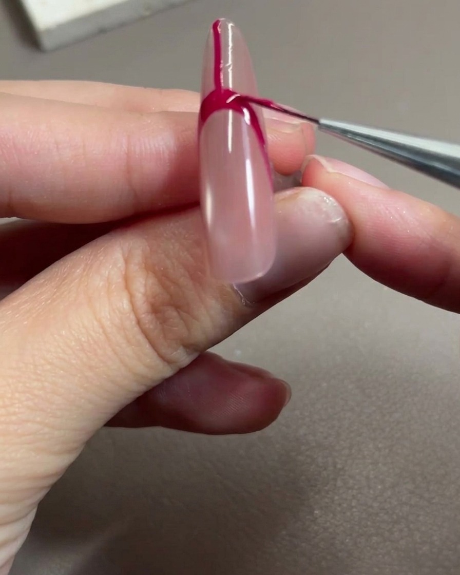 Un pincel de arte de uñas aplicando gel rojo rosa para rellenar el espacio dentro del contorno de la francesa.