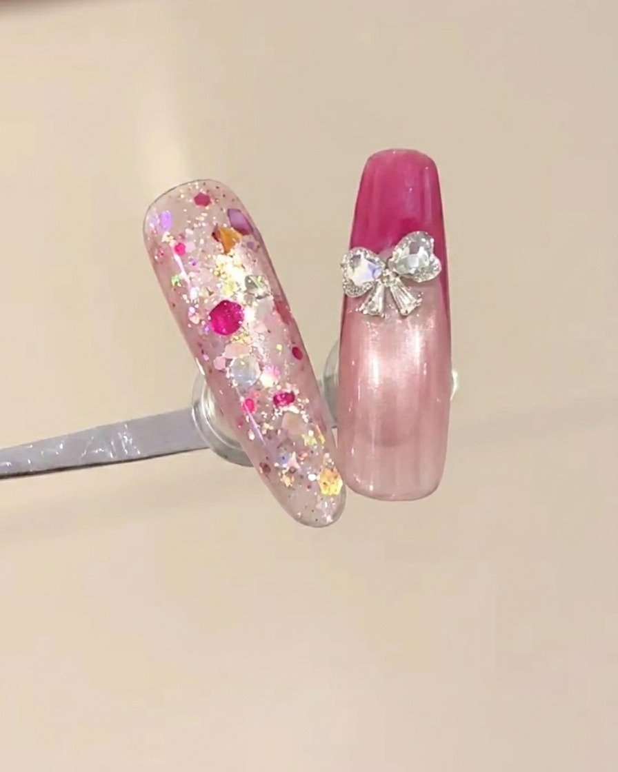 Dos pequeñas piedras de strass en forma de corazón siendo colocadas en la base de la punta francesa para crear un diseño de lazo.