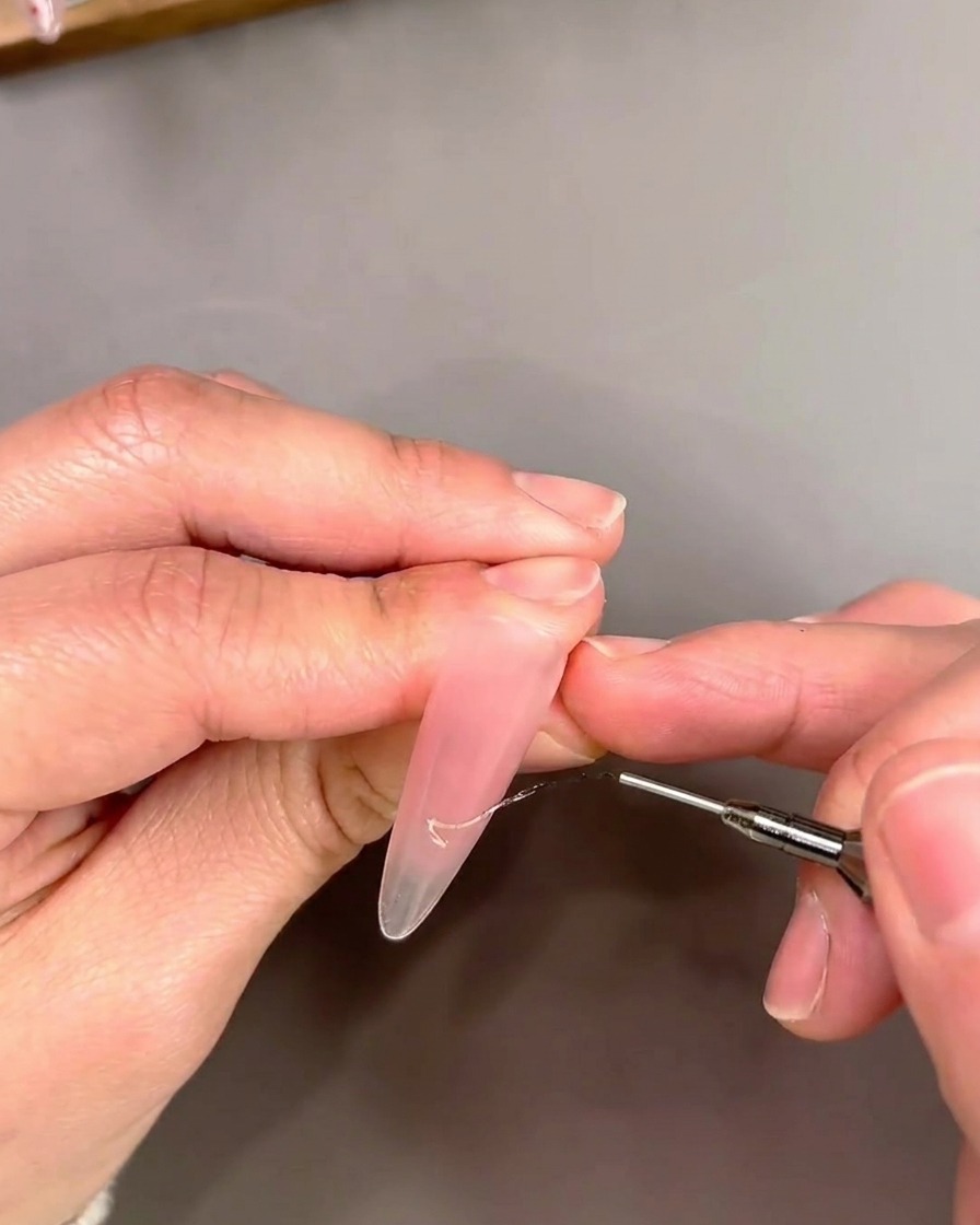 Primer plano de un pincel liner aplicando gel cat-eye dorado en un diseño de punta francesa.