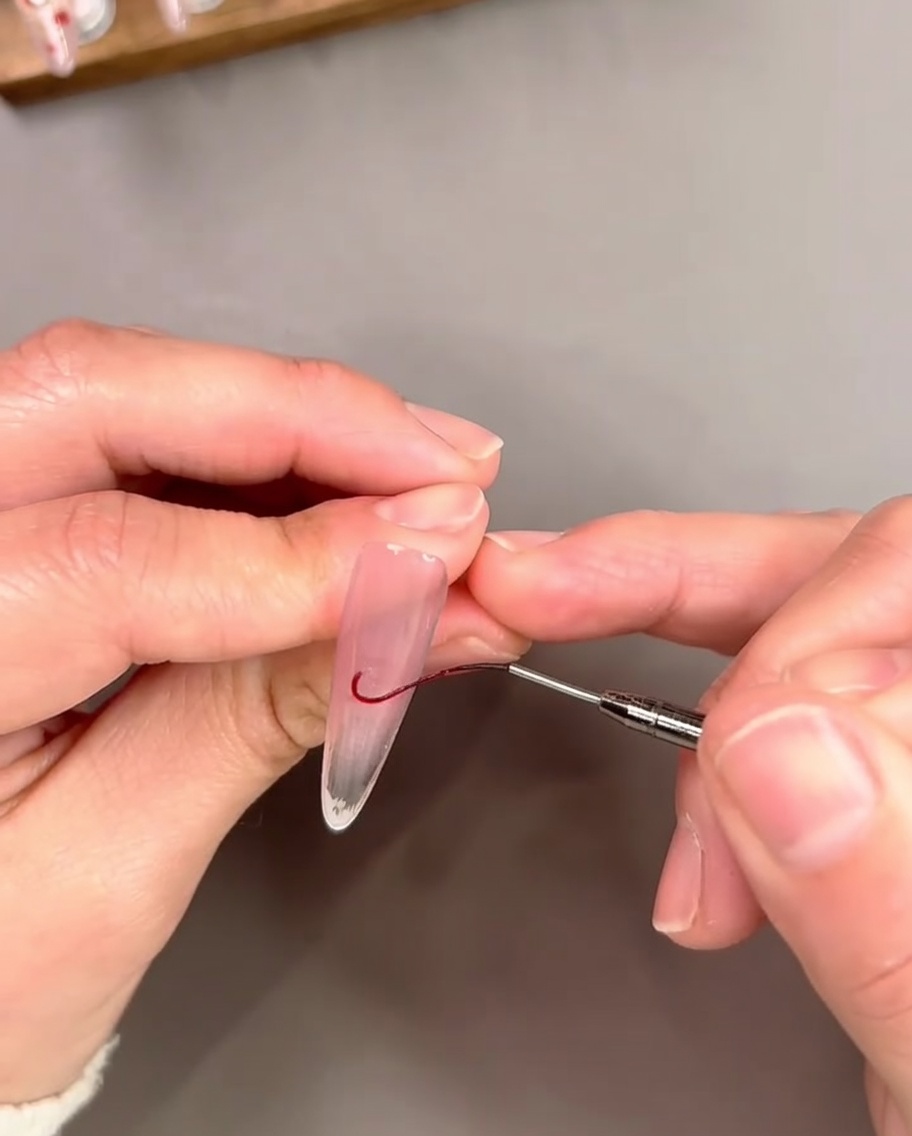 Un pincel liner fino dibujando una línea curva de gel rojo cerca del borde libre para delinear una punta francesa.